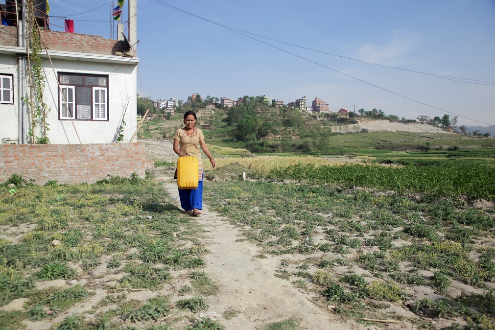 Rasmina's mother, Sanchakumari Tamang, walks to her house after she filling a jerry can with water the nearby well. Photo Credit: Mithila Jariwala