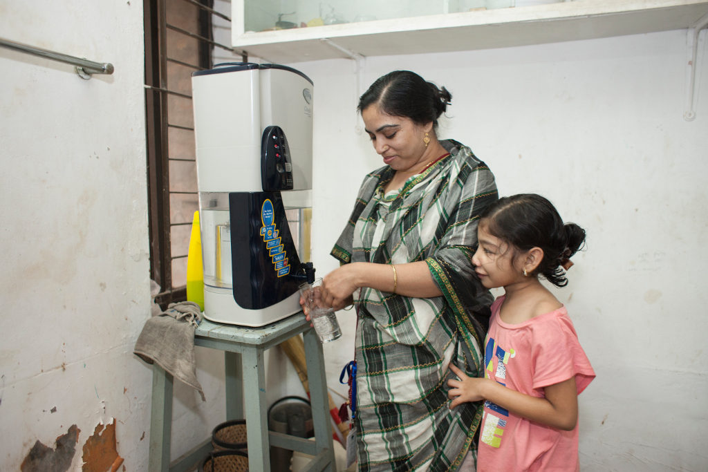 Nishita’s mother, Rehana, helps her with a glass of water. The family drinks from a water filter in their household. Photo credit: Suvra Kanti Das