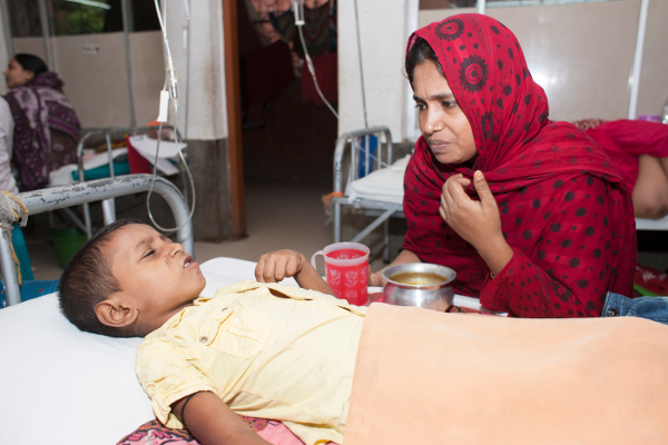 Hasina struggles to convince Samir to take some food and drink. Severe loss of appetite is a common symptom of typhoid.