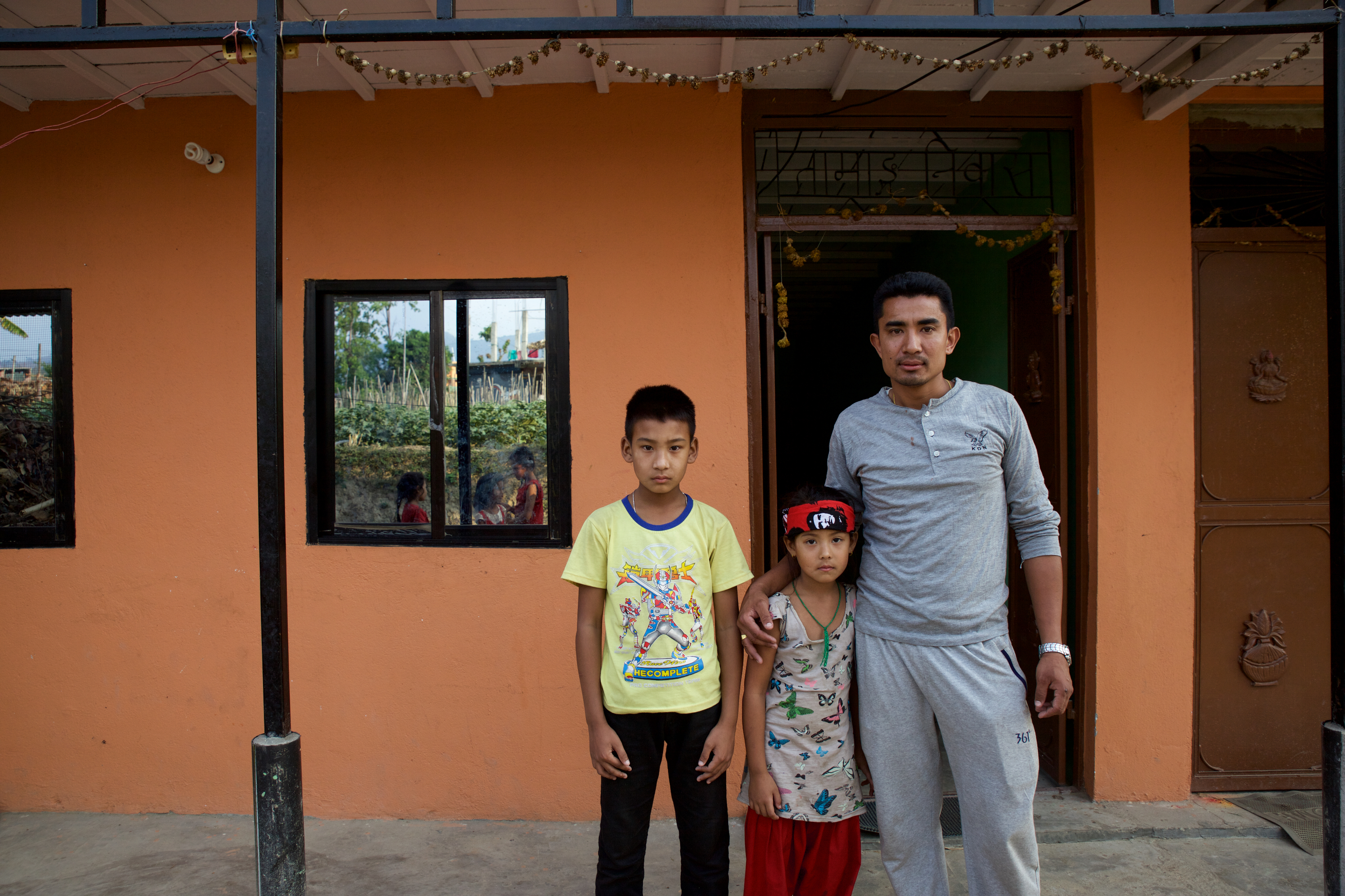 Ayush, Ayusha and Ram in front of their family home. After the devastating 2015 earthquake in Nepal, the Lama family rebuilt their home from wood and stone, taking out a loan to ensure their children were safe from future earthquakes..