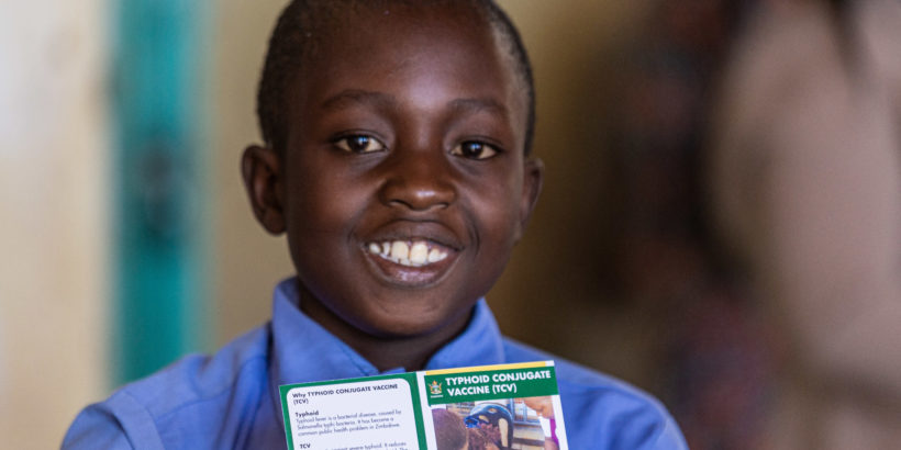 A young boy smiles with his vaccination card after receiving typhoid conjugate vaccine in Zimbabwe