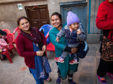 Two women smile while holding a baby