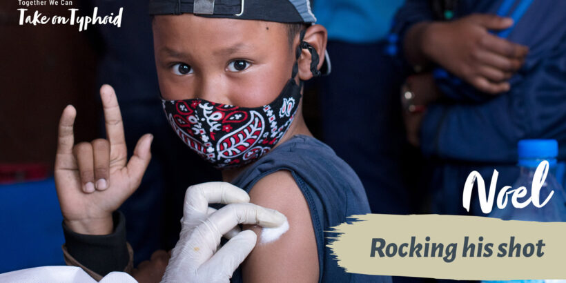 Boy wearing mask making rock n roll gesture as he receives a vaccine. text: "Noel: Rocking his shot"