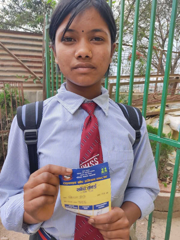 Girl wearing a backpack holds vaccination card