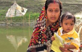 Woman holds a young child with a vaccination card, with water in the background