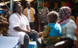 A health care worker in a medical uniform speaks to a woman holding her child during a typhoid conjugate vaccine campaign in Burkina Faso.