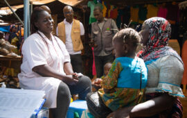 A health care worker in a medical uniform speaks to a woman holding her child during a typhoid conjugate vaccine campaign in Burkina Faso.