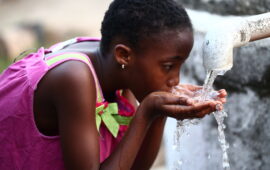 A young girl drinks from a makeshift handpump in Liberia. WASH and vaccines are complementary interventions that can work together to prevent waterborne diseases.