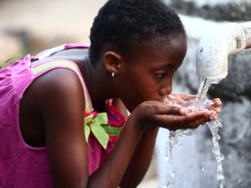 A young girl drinks from a makeshift handpump in Liberia. WASH and vaccines are complementary interventions that can work together to prevent waterborne diseases.