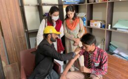 A man in a yellow hard had administers the typhoid conjugate vaccine to a boy in Pakistan in 2022. Pakistan's final TCV campaign followed unprecedented floods in July 2022 that compromised WASH infrastructure and disrupted access to health services across the country.