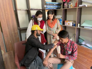 A man in a yellow hard had administers the typhoid conjugate vaccine to a boy in Pakistan in 2022. Pakistan's final TCV campaign followed unprecedented floods in July 2022 that compromised WASH infrastructure and disrupted access to health services across the country.
