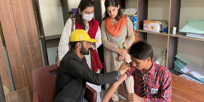 A man in a yellow hard had administers the typhoid conjugate vaccine to a boy in Pakistan in 2022. Pakistan's final TCV campaign followed unprecedented floods in July 2022 that compromised WASH infrastructure and disrupted access to health services across the country.