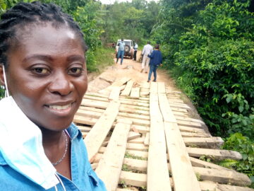 Patience Dapaah, a senior advocacy and communications advisor at PATH, stands with several team members as they inspect a wooden bridge in a forest in Liberia.