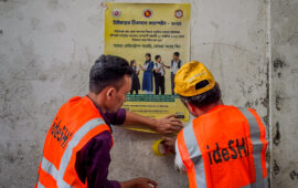 Two campaign workers wearing orange vests put up a sign with information about the typhoid conjugate vaccine in Bangladesh.