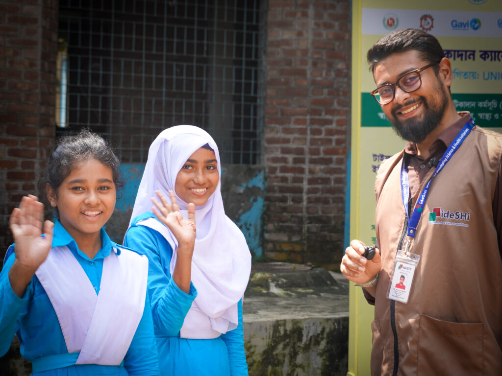 An ideSHi campaign worker stands with two children during Bangladesh’s TCV introduction campaign.